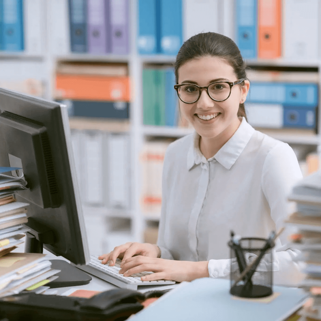 Smiling woman working at her cluttered office desk with a computer.