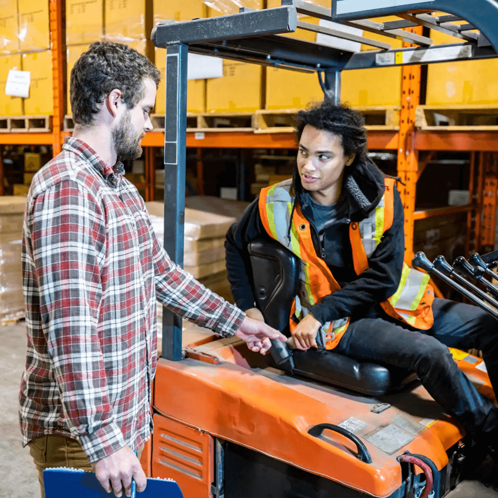 Two warehouse workers discussing on a forklift.