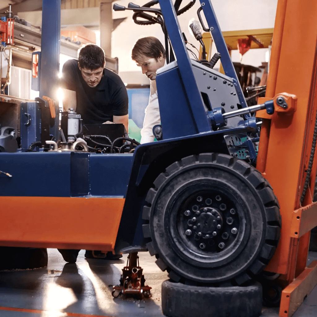 Two workers inspecting and repairing a forklift in a workshop.