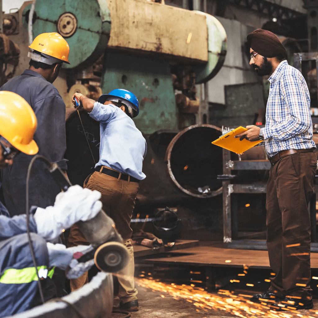 Workers wearing safety helmets operating machinery and grinding metal.
