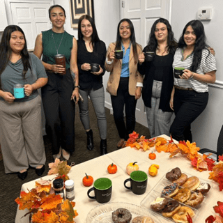A group of six women holding drinks and smiling around a festive fall-themed table.
