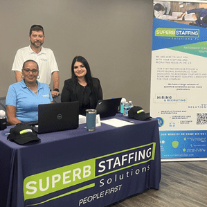 Three people at a staffing solutions booth with laptops and promotional materials.
